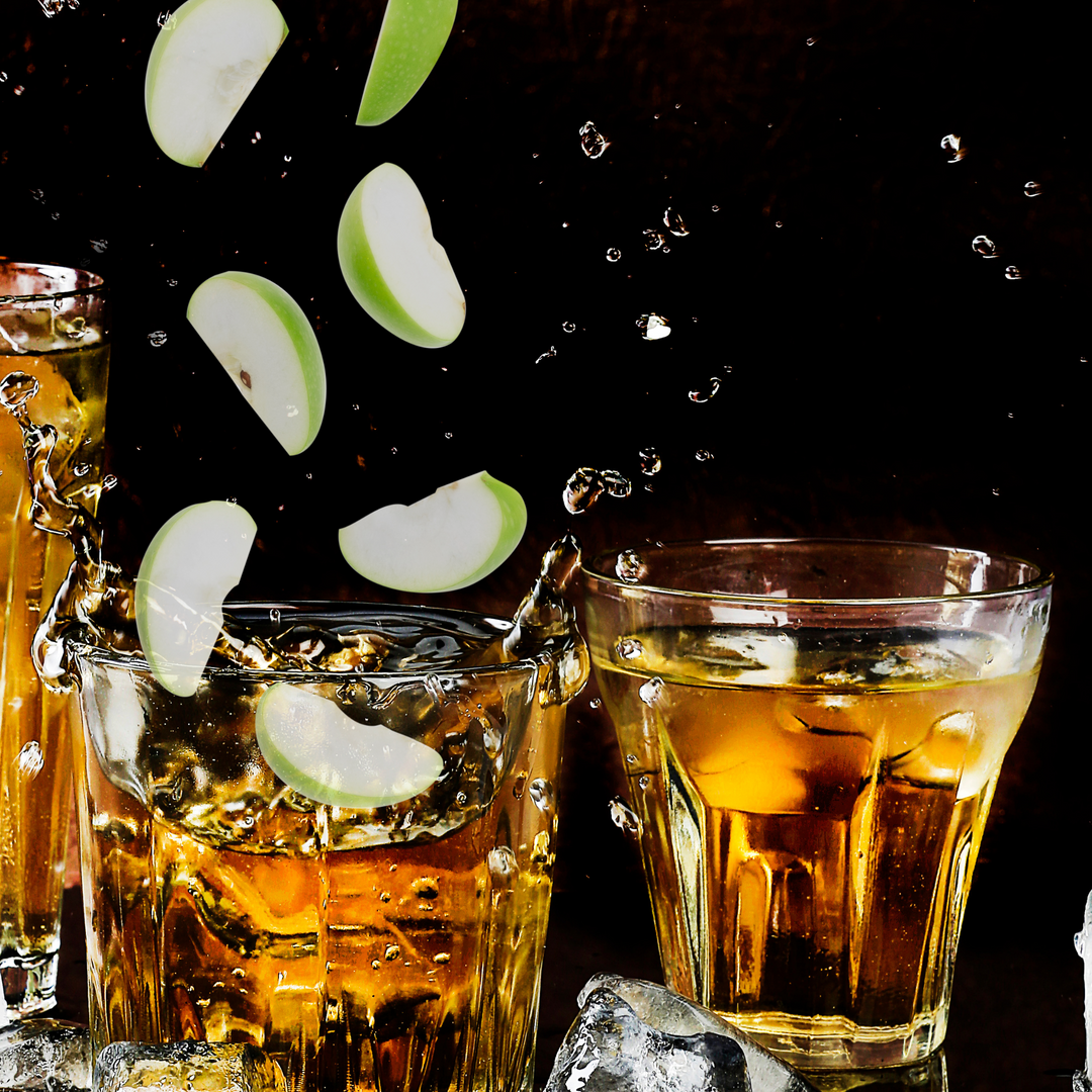 green apples splashing into glasses of bourbon