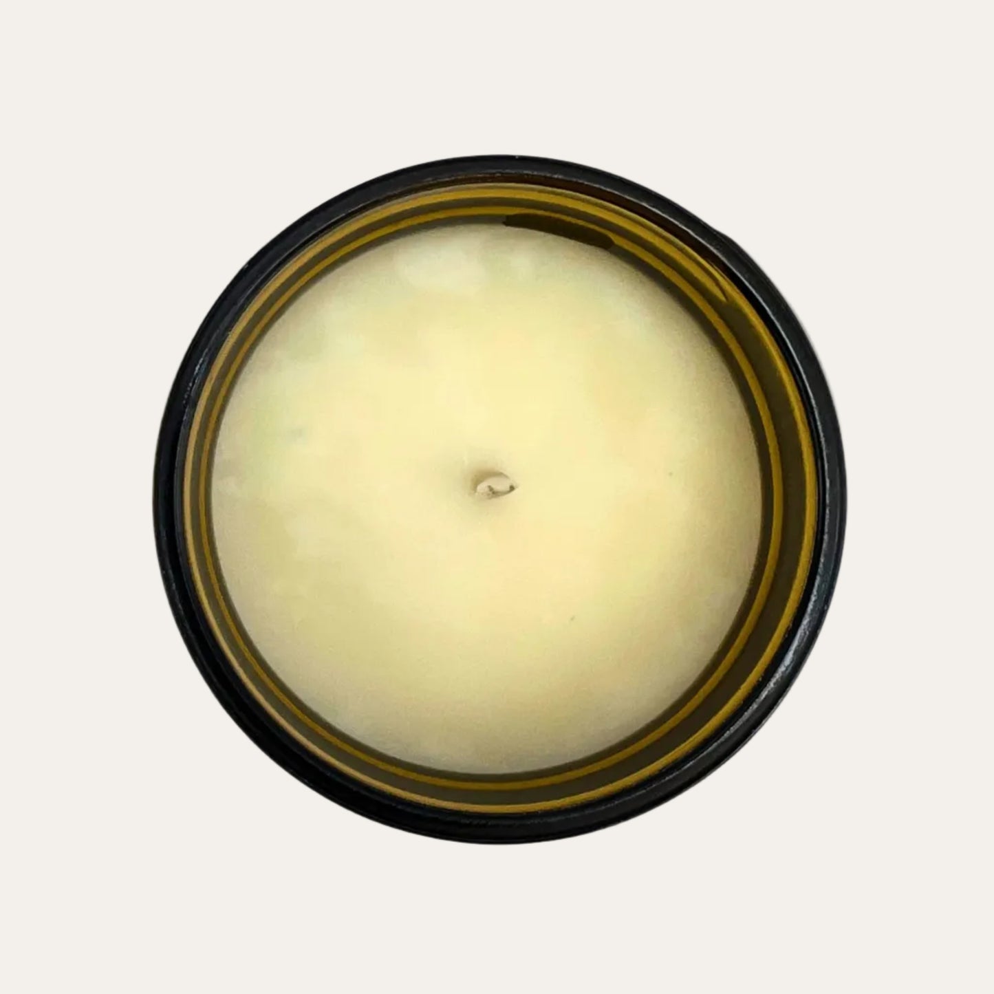 Round candle with a wick and amber container on a cream background