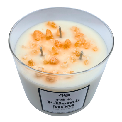 Candle in a glass jar labeled 'F-Bomb Mom' with decorative elements on a white background