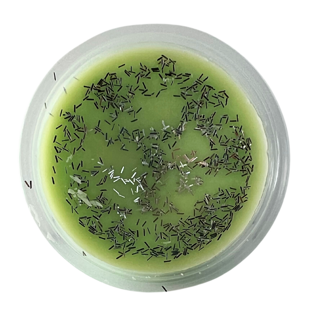 Green wax tart in a round shot cup with silver glitter. White background.